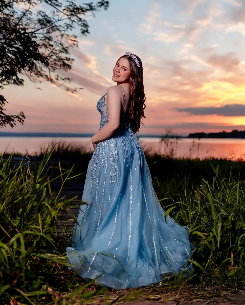Quinceañera de pie con vestido azul al atardecer