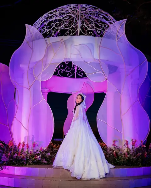 Quinceañera bajo un arco de flores violetas